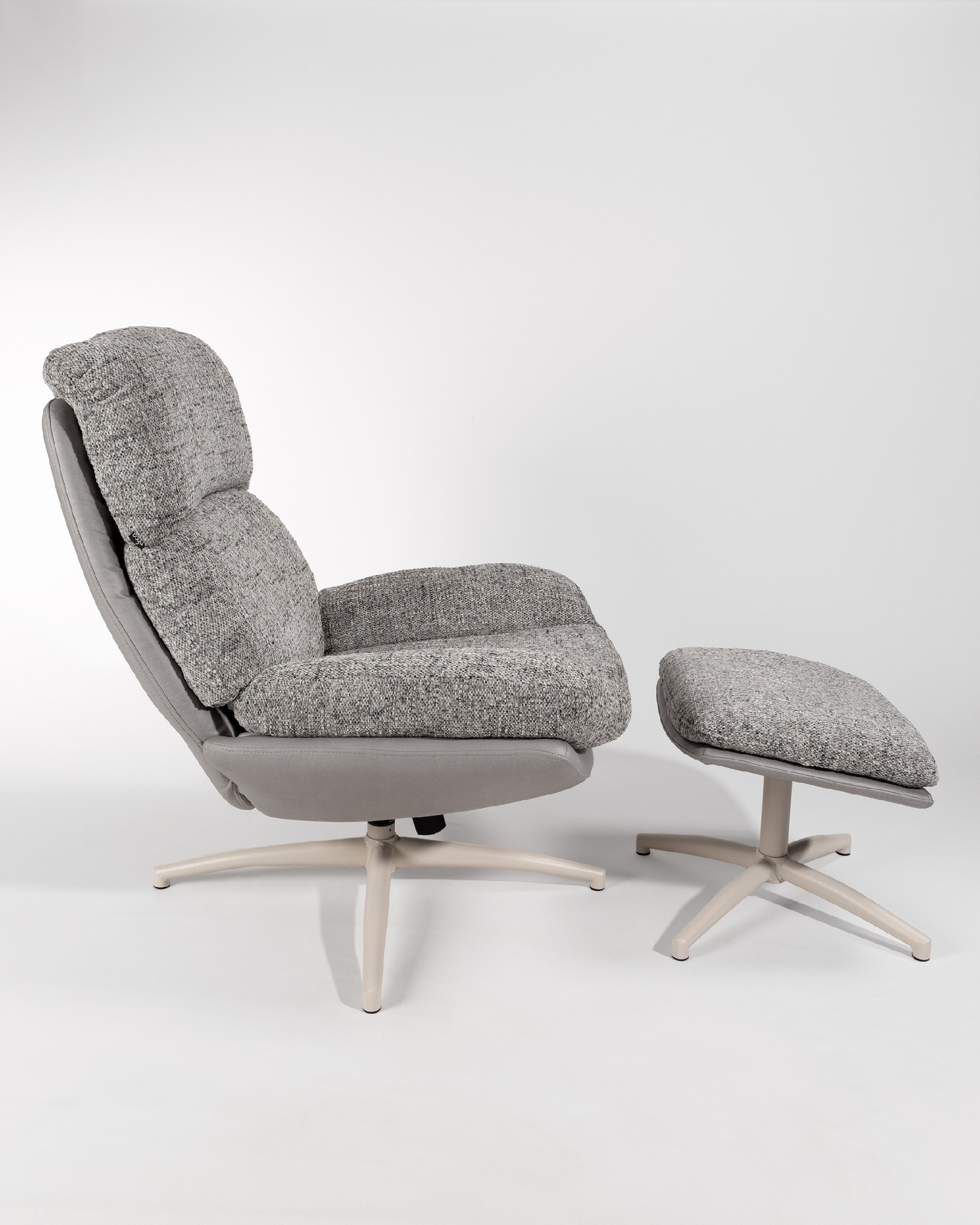Fauteuil Fresia avec un revêtement gris et tempête avec un pouf à structure métallique ivoire, basculant et rotatif à 360°.